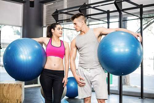 Fit couple posing with sport ball at crossfit gym