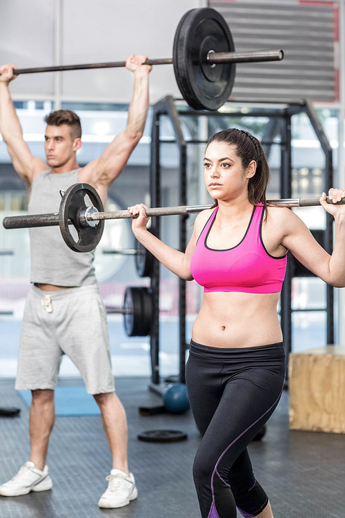 Fit couple lifting barbell at crossfit gym