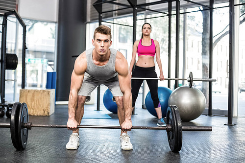 Fit couple lifting barbell at crossfit gym