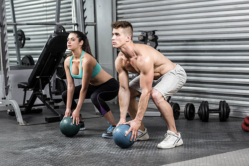 Fit couple doing ball exercise at crossfit gym