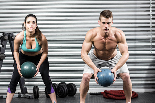 Fit couple doing ball exercise at crossfit gym