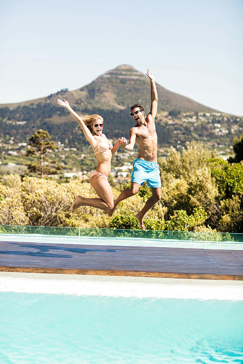 Happy couple jumping in the pool in a sunny day