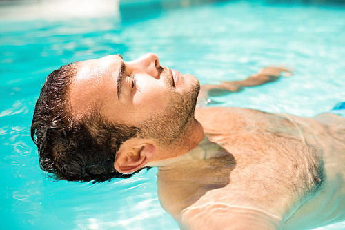 Peaceful man floating in the pool with closed eyes