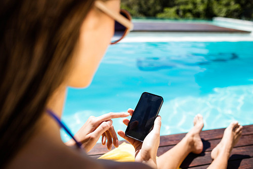 Over shoulder view of brunette using smartphone poolside