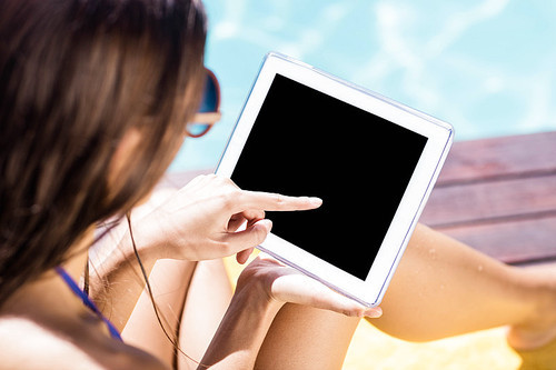 Over shoulder view of brunette using tablet poolside