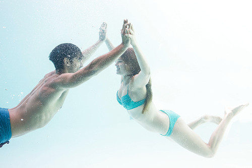 Smiling couple under water putting hands together