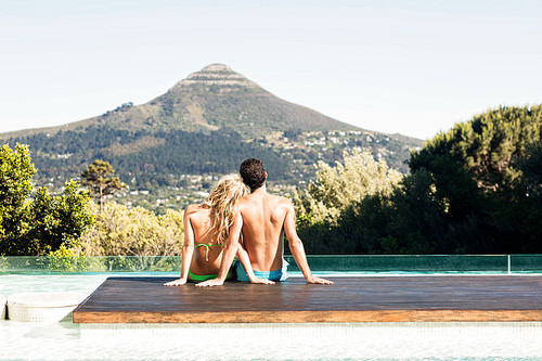 Rear view of couple sitting bu the pool looking at the landscape