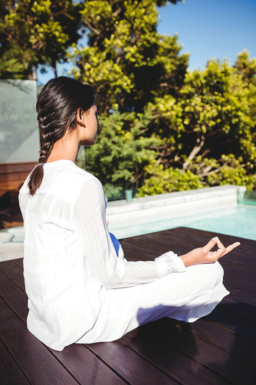 Calm brunette doing yoga by the pool