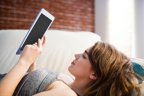 Pretty woman lying on the couch using her tablet in the living room