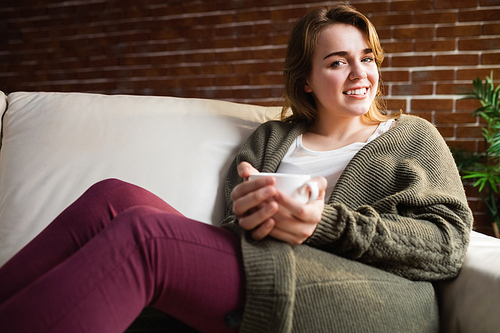 Pretty woman drinking coffee lying on the couch in the living room