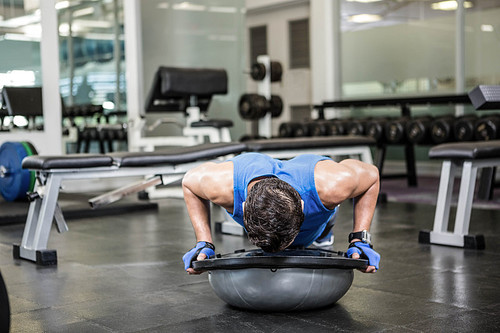 Muscular man doing push up with bosu ball at the gym