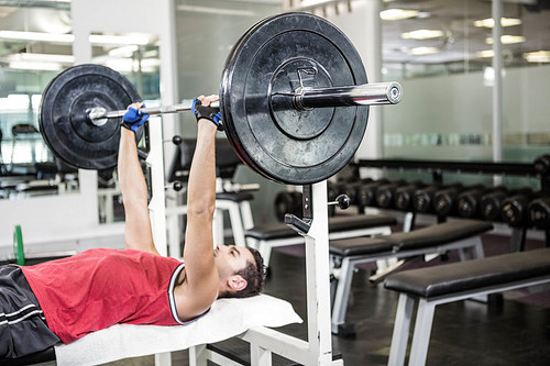 Muscular man lifting barbell on bench at the gym