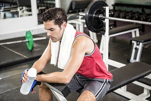 Tired man sitting on bench holding bottle of water in the gym