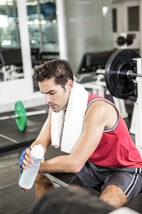 Tired man sitting on bench holding bottle of water in the gym