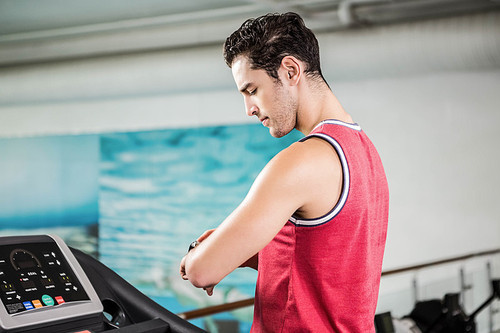 Serious man on treadmill looking at smart watch in the gym