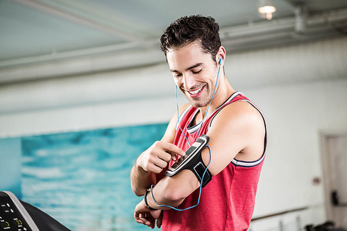 Smiling man on treadmill using smartphone in the gym
