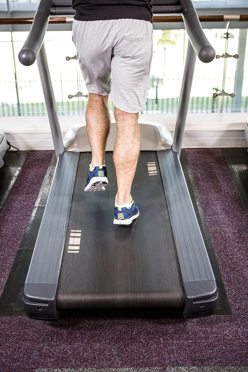 Lower section of fit man running on treadmill at the gym