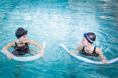 Smiling women in the pool with foam rollers at the leisure center