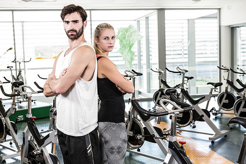 Fit couple standing back to back with arms crossed at the gym