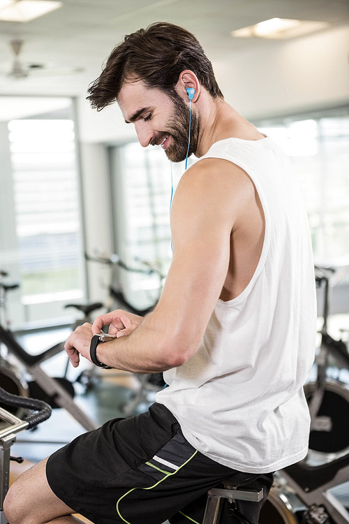 Smiling man on exercise bike using smartwatch at the gym