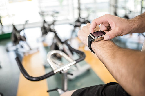Close up of man using smartwatch on exercise bike at the gym