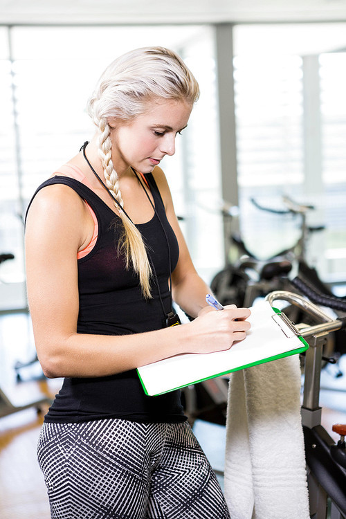 Smiling female trainer writing on clipboard at the gym