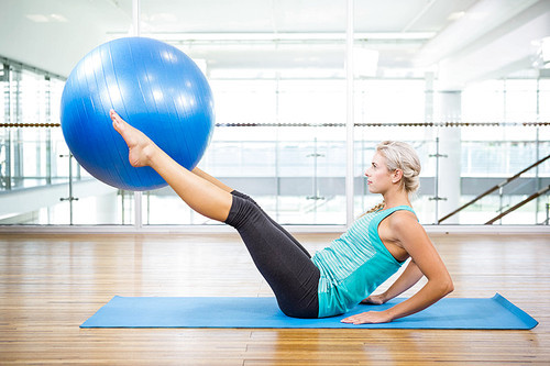 Fit blonde on mat holding with legs fitness ball in the studio