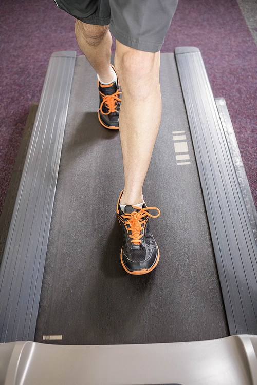 Lower section of man running on treadmill at the gym