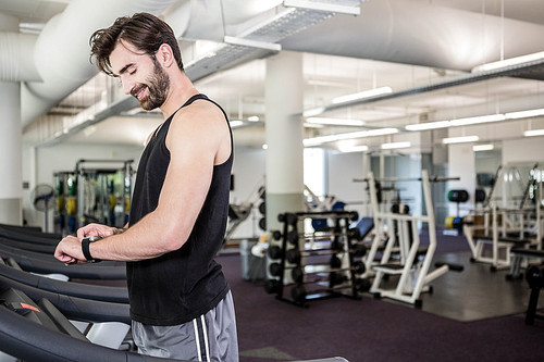 Smiling man on treadmill looking at smartwatch at the gym