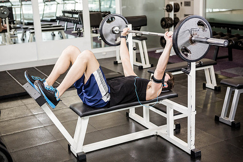 Muscular man lifting barbell on bench at the gym