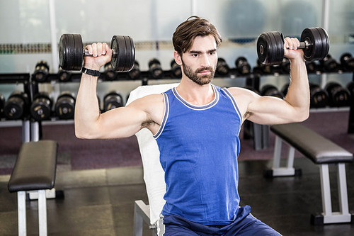 Muscular man lifting dumbbells on bench at the gym
