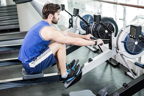 Handsome man doing exercise on drawing machine at the gym