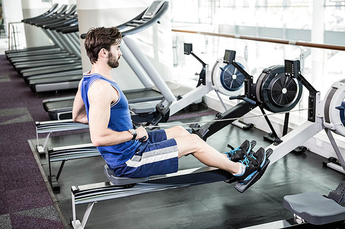 Handsome man doing exercise on drawing machine at the gym