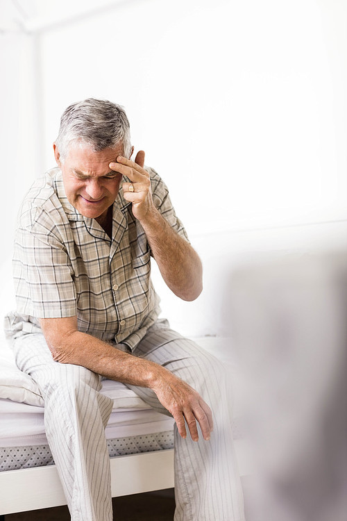 Suffering senior man touching his forehead at home