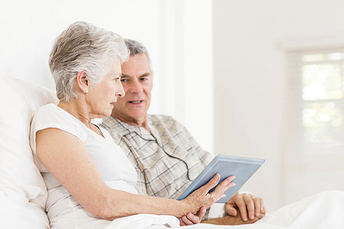 Senior couple using tablet sitting on bed