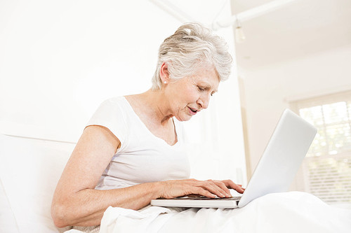 Mature woman using laptop sitting on bed