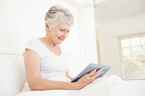 Smiling woman using tablet sitting on the bed