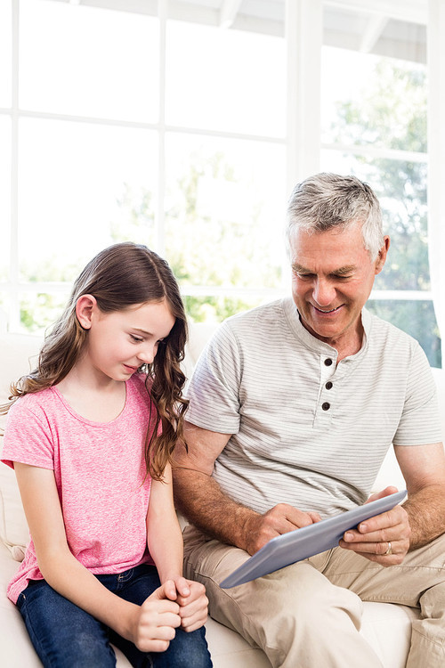 Smiling grandfather and granddaughter using tablet on the sofa