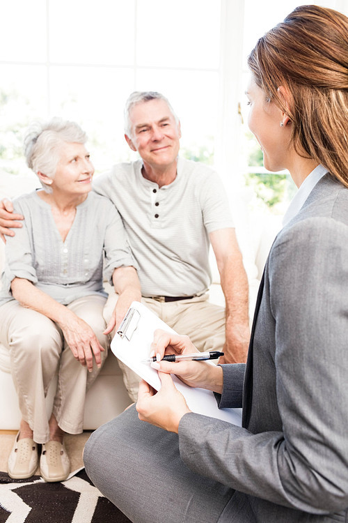 Businesswoman talking with senior couple and writing on clipboard at home