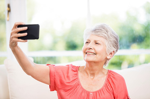 Happy senior woman taking selfie on the sofa