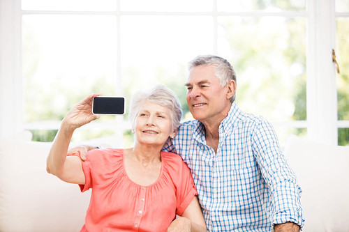 Happy senior couple taking a selfie on the sofa