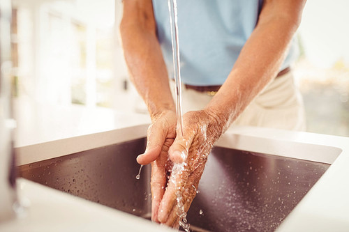 Mid section of senior man washing hands in the kitchen