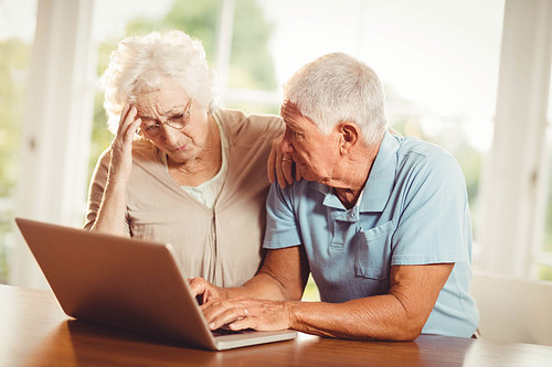 Worried senior couple using laptop at home