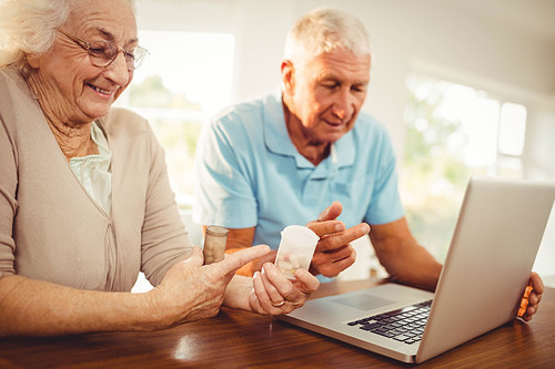 Senior couple using laptop and holding pills at home