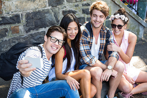 Hip friends taking selfie while sitting on sidewalk