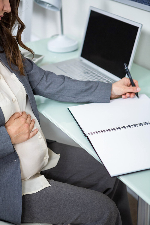 Pregnant businesswoman writing in folder in home office