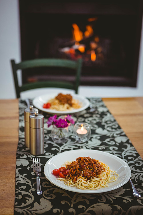 Plates of spaghetti on table next to fireplace