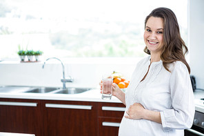Pregnant woman holding a glass of water in kitchen