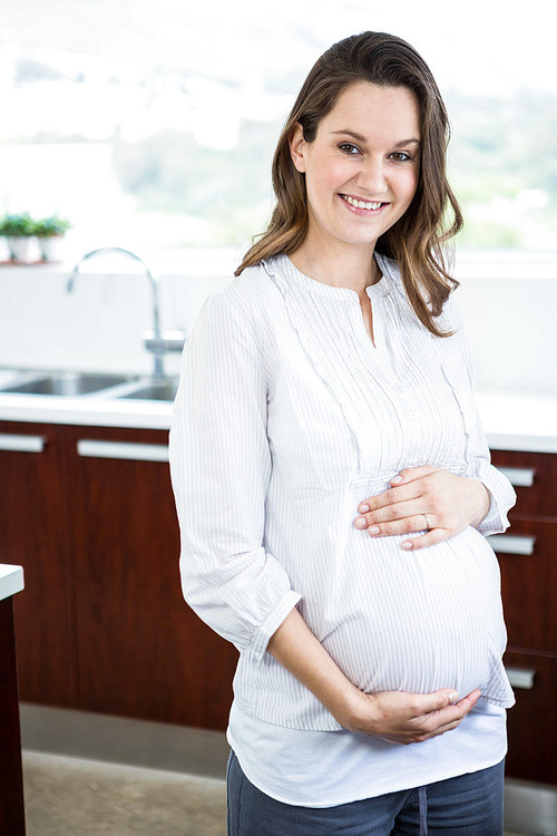 Pregnant woman touching her belly in kitchen
