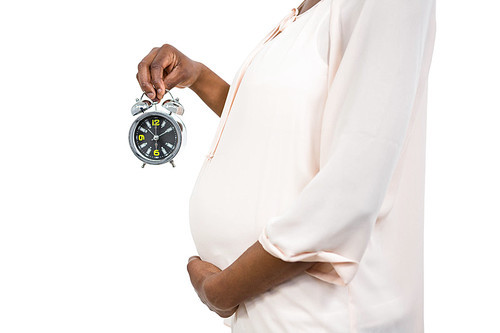 Pregnant woman holding an alarm clock on white background